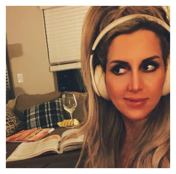 Dr. Brownlee sitting on her couch with headphones, reading a book, and drinking a glass of wine