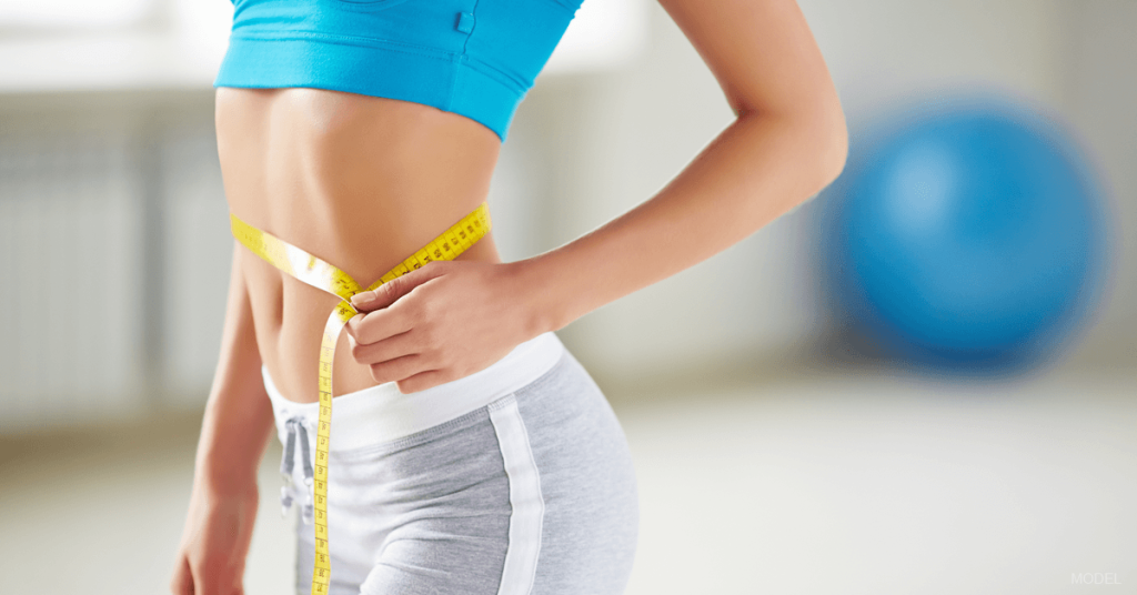 A woman measures her waist after undergoing and recovering from a tummy tuck procedure.