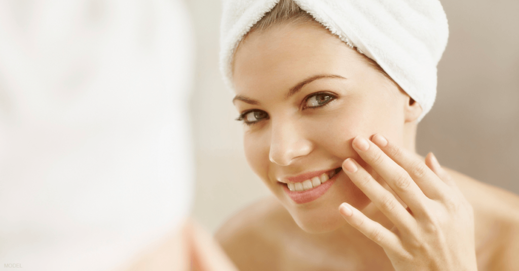 A woman looks in the mirror after a shower to observe her smooth, radiant skin following a chemical peel.