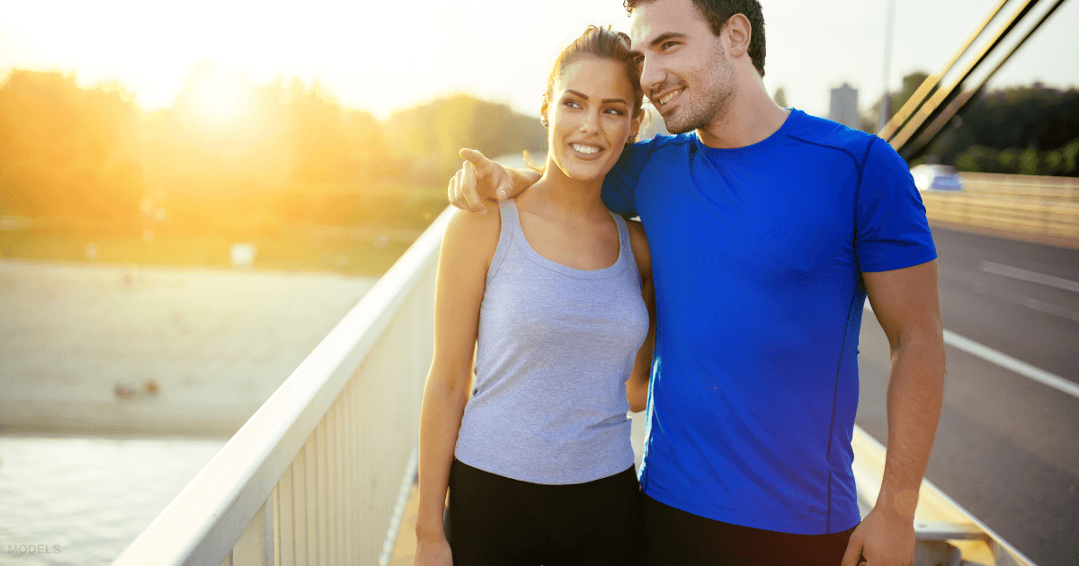 A woman and man walk across a bridge at sunset.