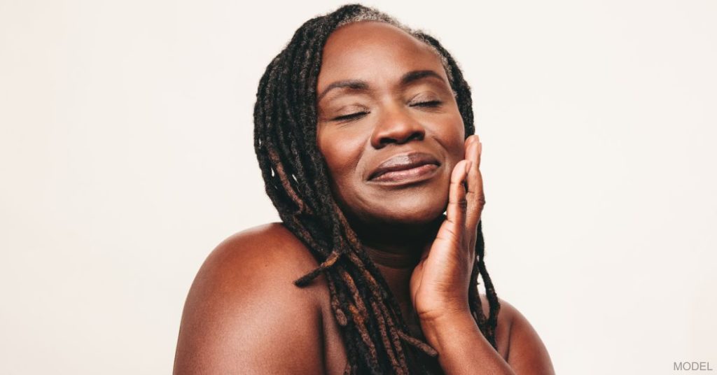 A woman with her eyes closed and touching her cheek (model)