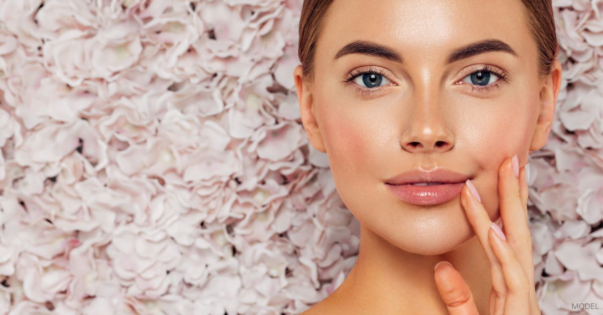 Woman with beautiful skin (model) in front of a wall of flowers.